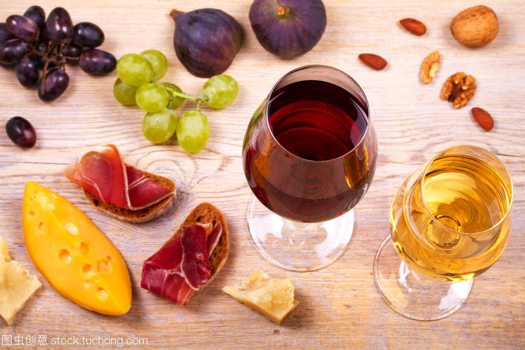 紅色和白色奶酪、 火腿、 無花果和葡萄與葡萄酒杯。木制的桌子上的酒杯。葡萄酒的靜物
